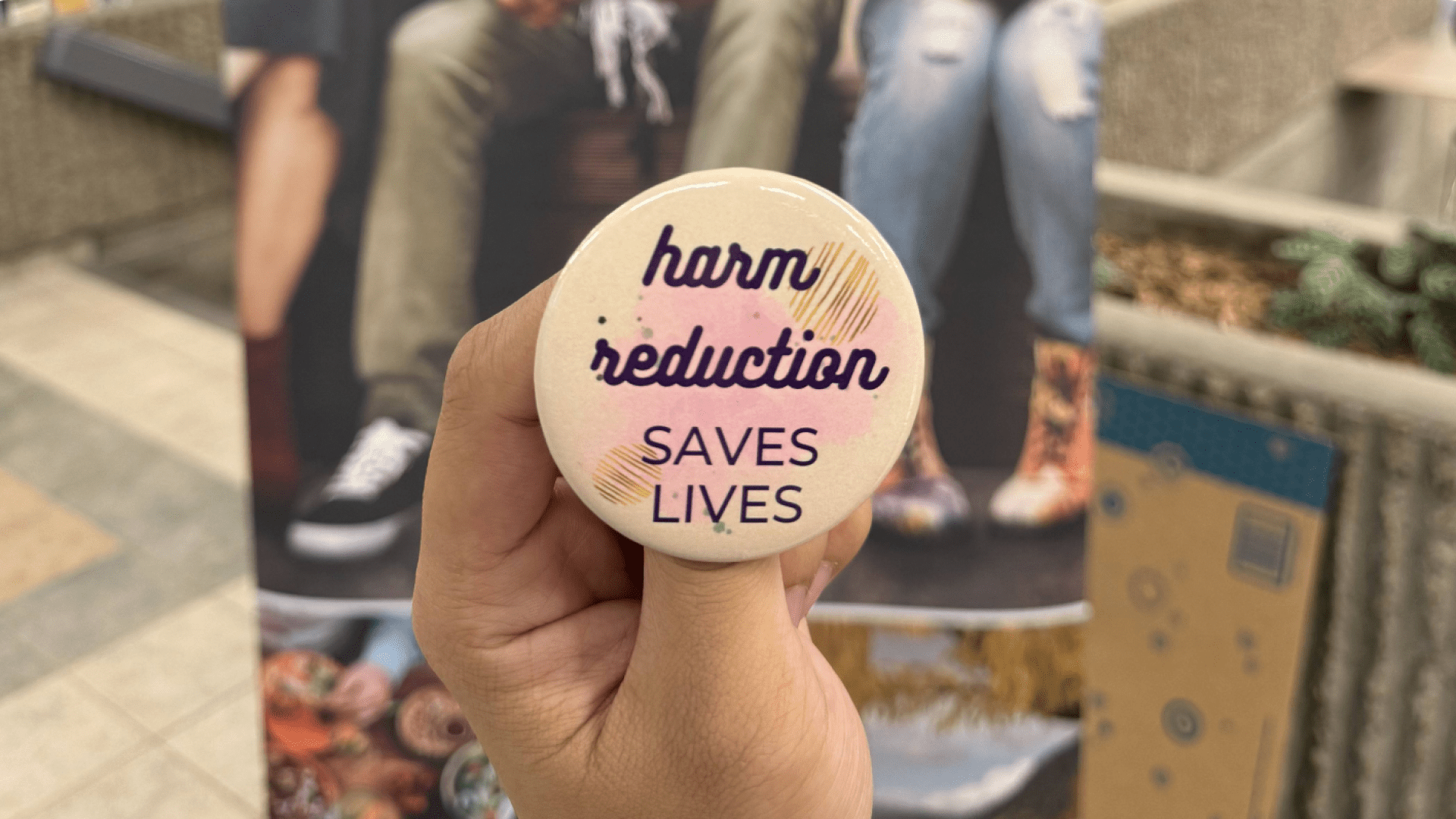 Student holds up a button that says Harm Reduction