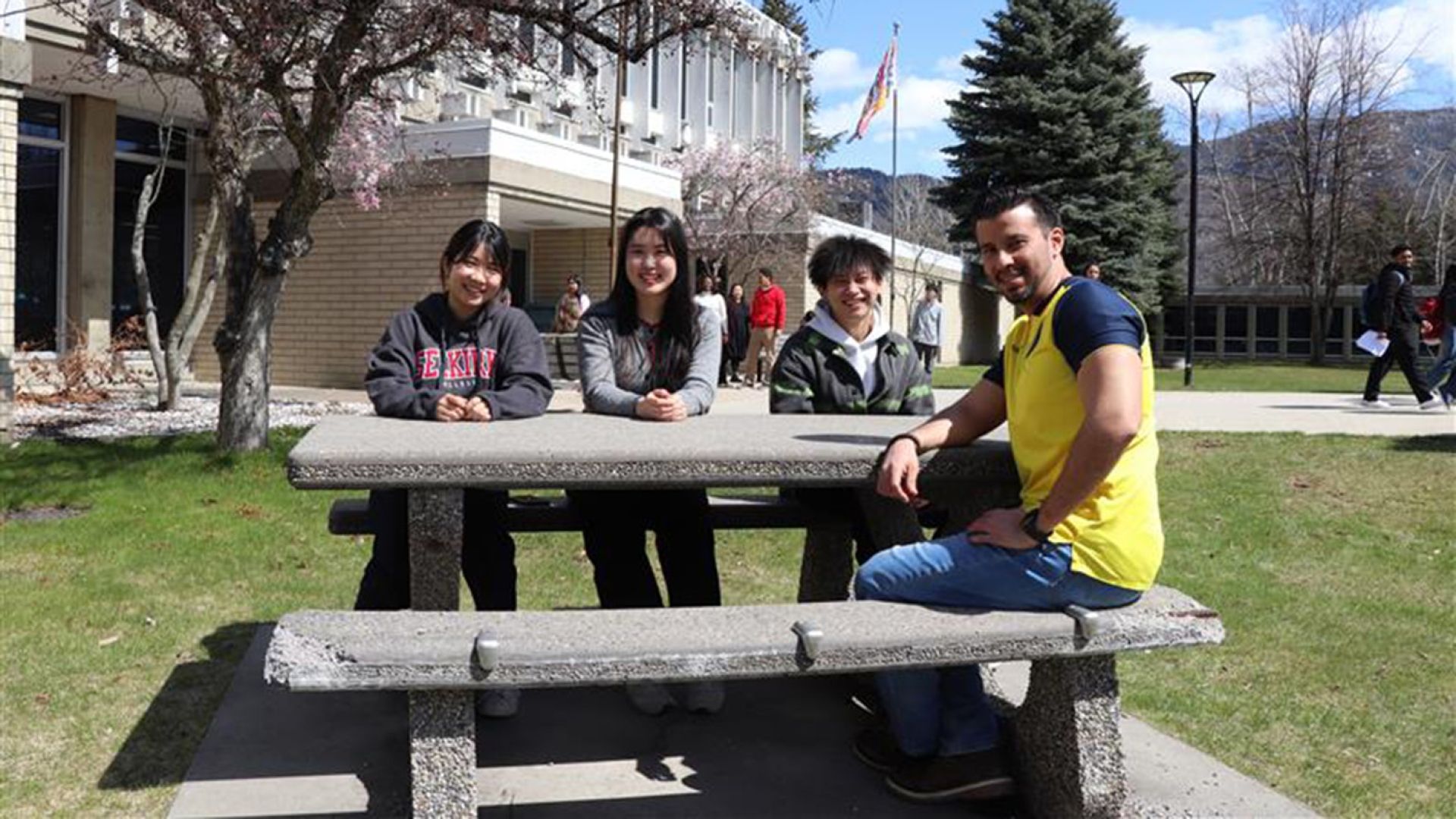 Four Selkirk College students sit outside on a picnic table in the sun