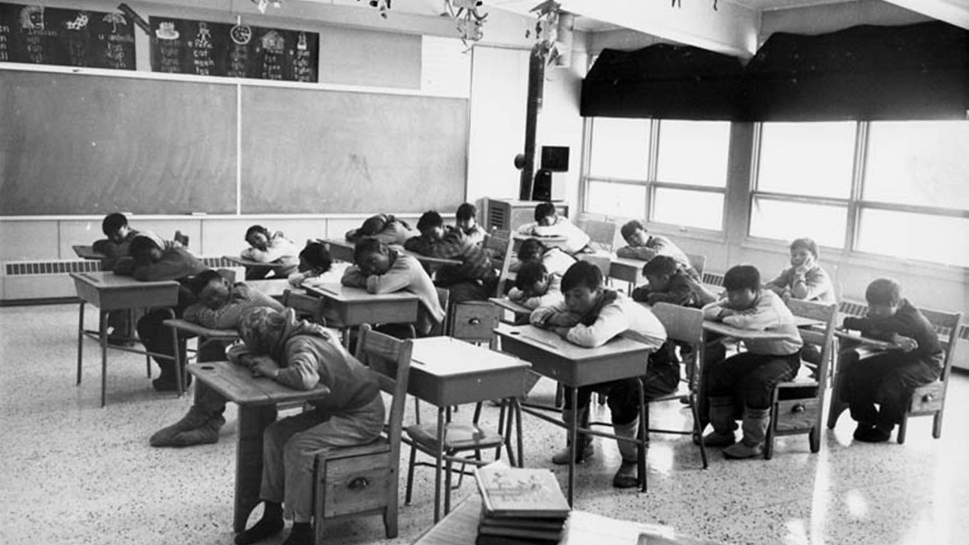Students seated in a classroom resting their heads on their desks, Cape Dorset (Kinngait) Federal Hostel, Nunavut