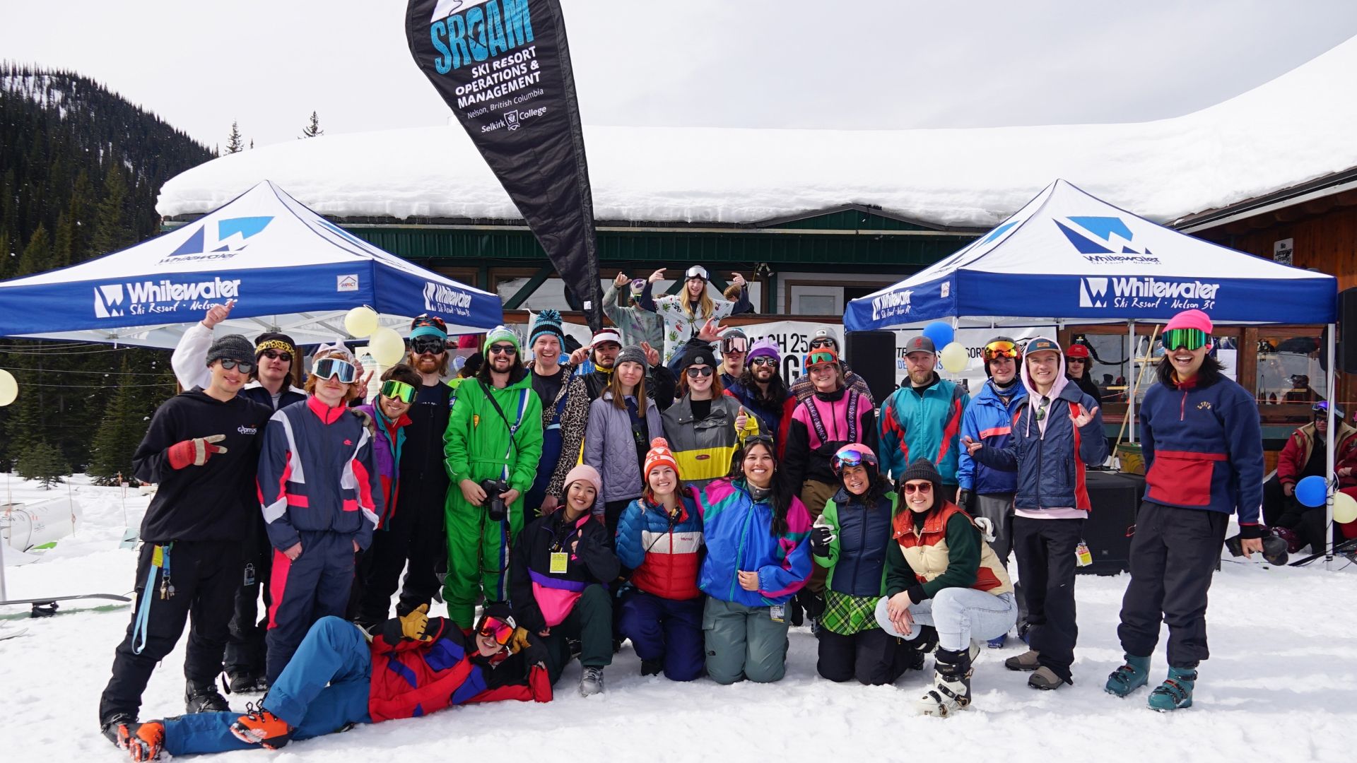 A group of Selkirk College Ski Resort Operations & Management students stand for a group photo in front of a lodge at Whitewater Ski Resort
