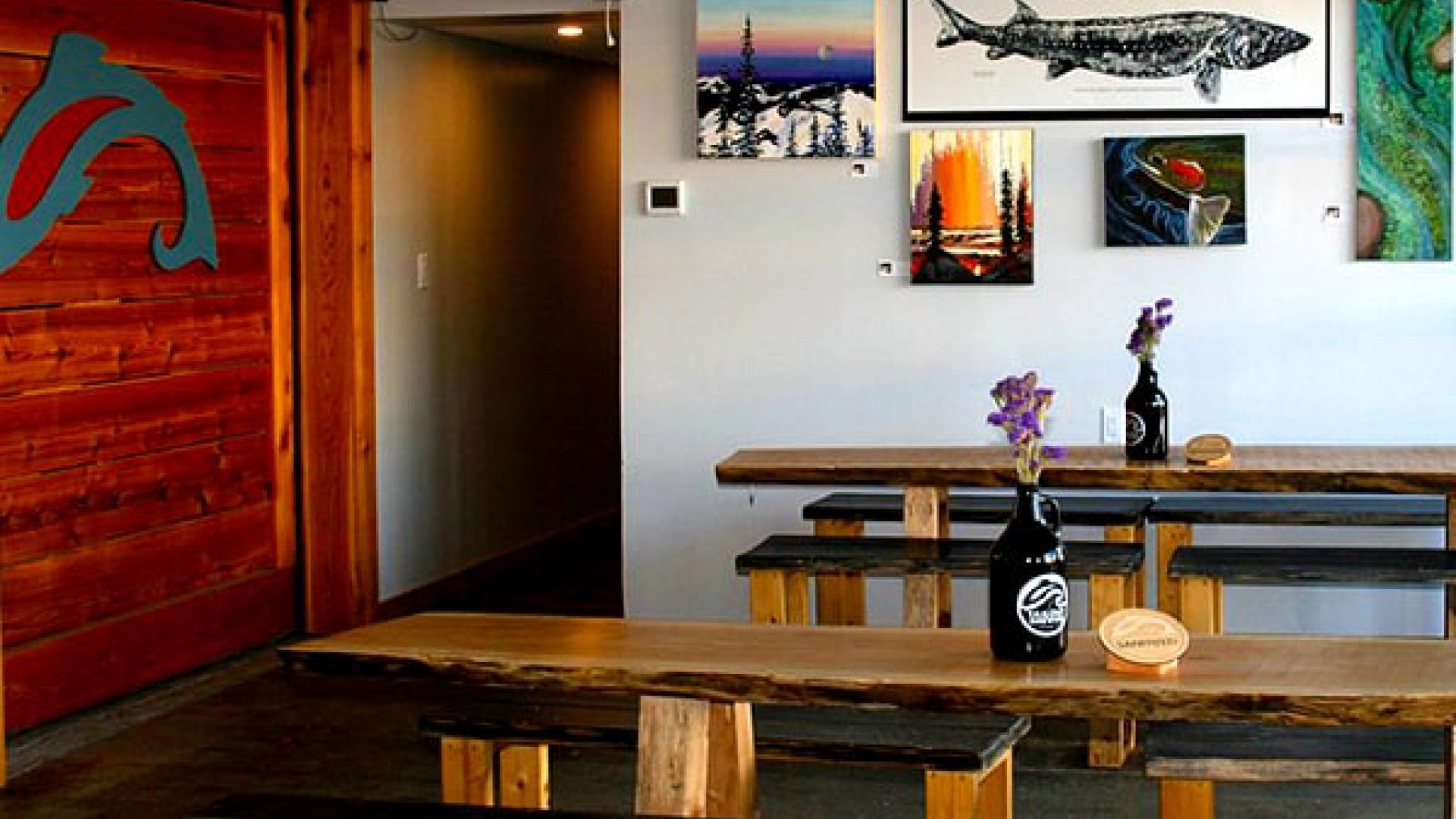 The inside of a brewery furnished with wooden tables art on the walls