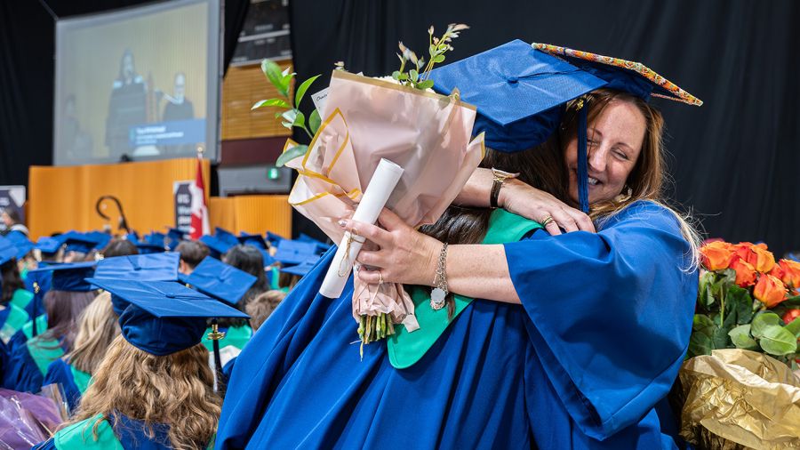 Students at Convocation hugging with flowers