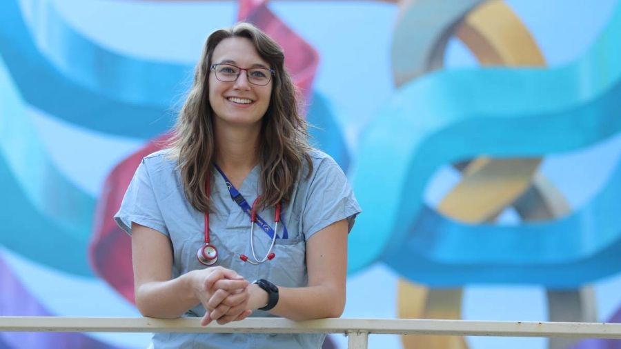 A student in scrubs stands in front of a mural