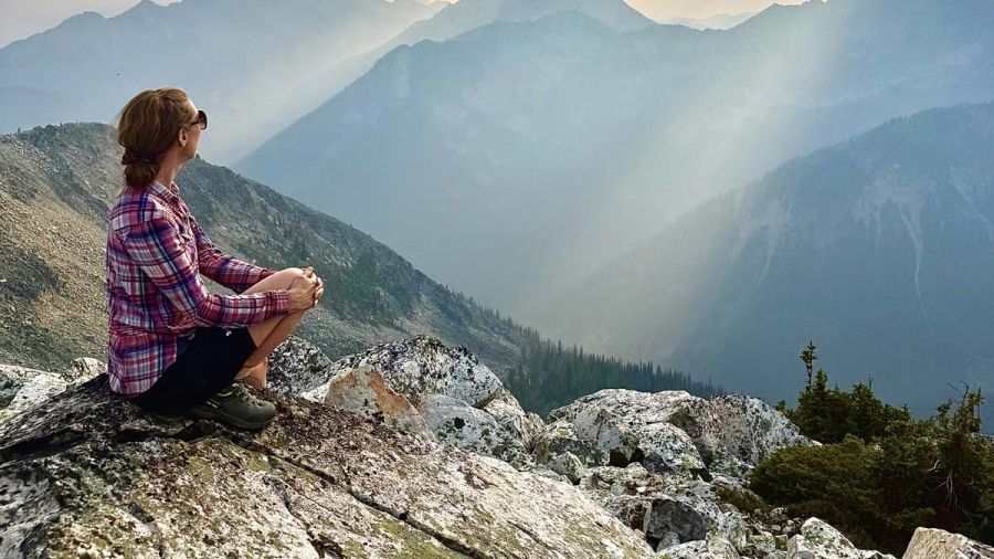 A hiker sits on a rock overlooking mountain ranges