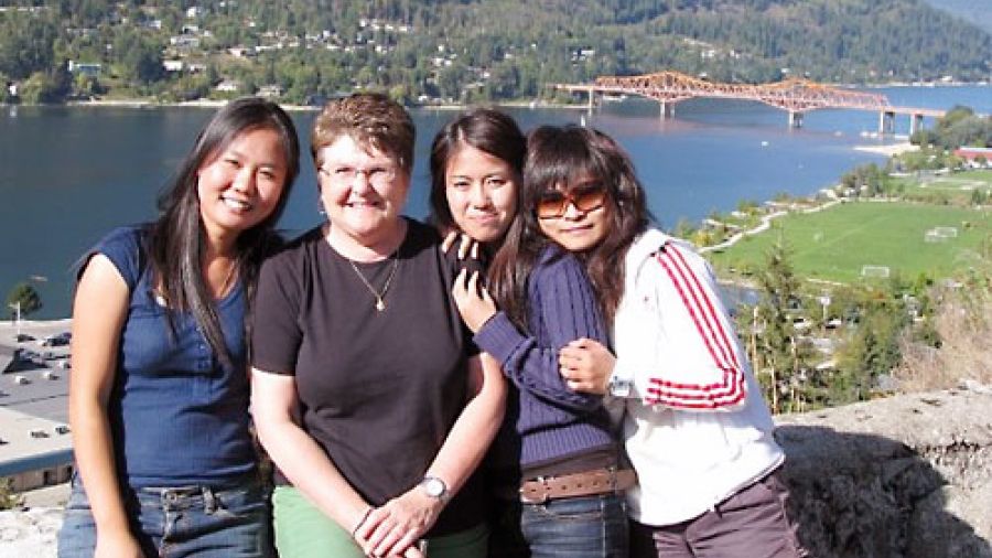 A group of people smile against the backdrop of Kootenay Lake and the Big Orange Bridge