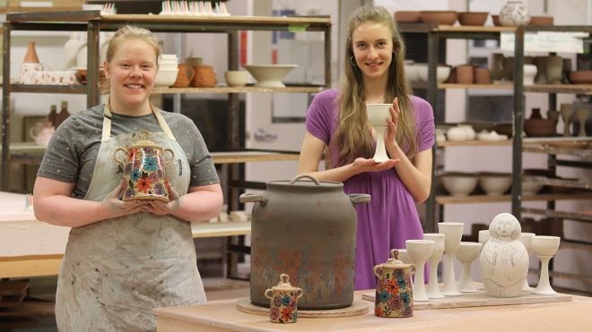 Two Ceramics Program students stand in the shop with their works that are in progress.