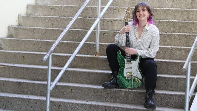 Class of 2024 co-valedictorian Jay Porteous sits on steps with her guitar.