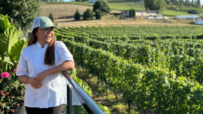 A person stands in vineyards smiling
