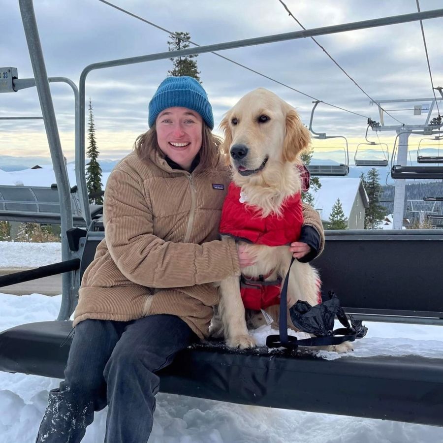 A woman sits on a chairlift holding a dog