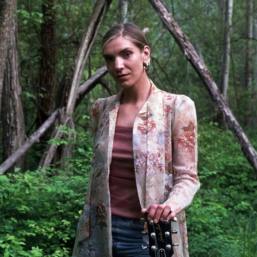 A woman standing in a forest holding a guitar