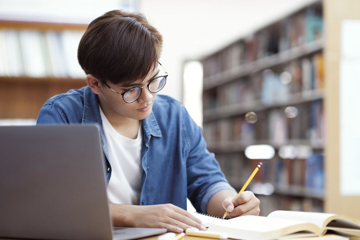 A student sits at a desk with books and a laptop