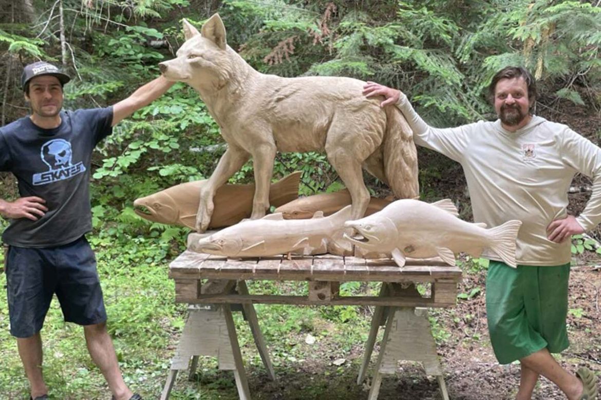 Two artists stand next to a carving of a coyote