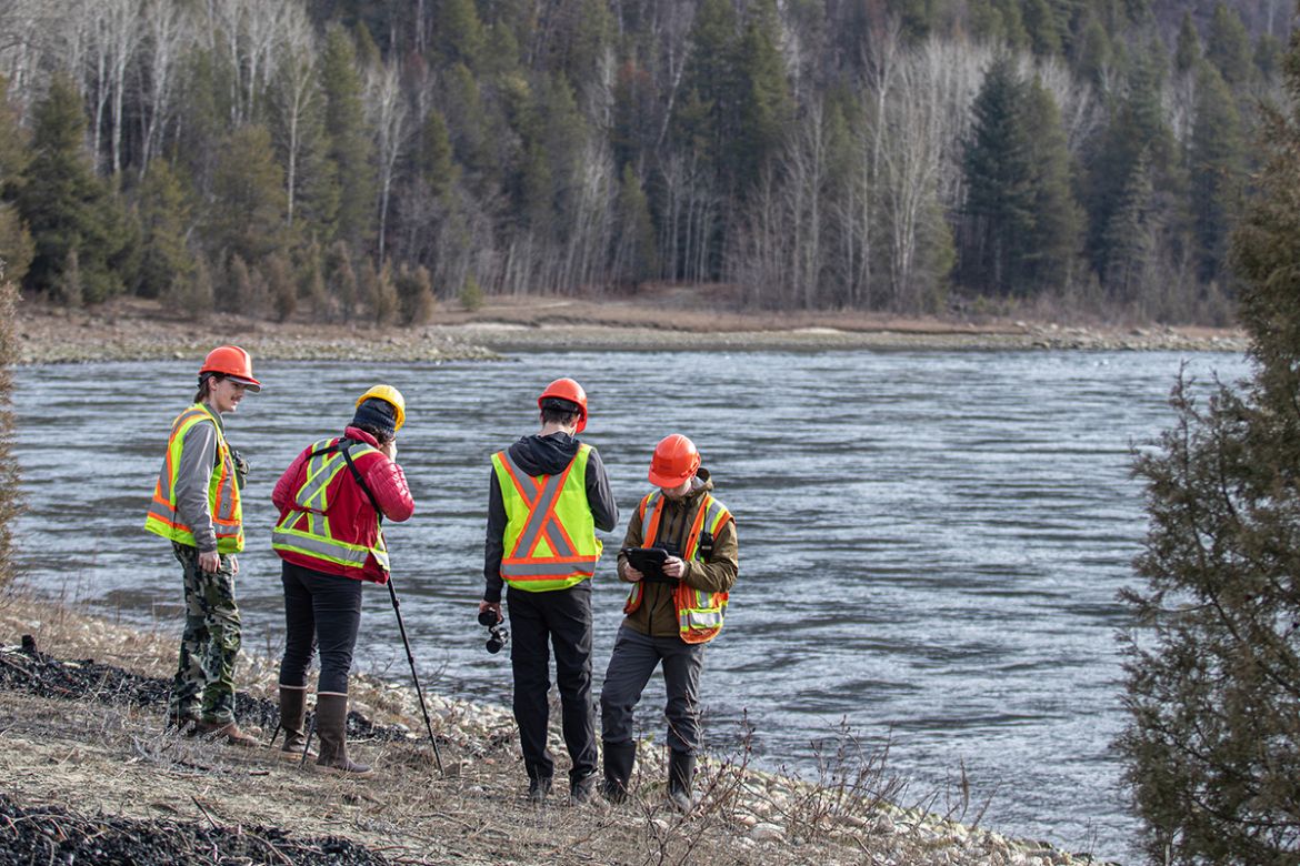 Students in high-vis vests stand on the banks of a lake with equipment