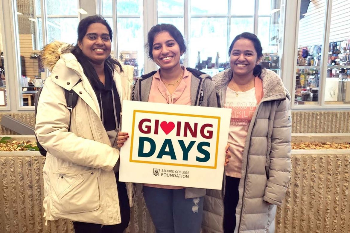 Three students stand holding a sign that reads "Giving Days"