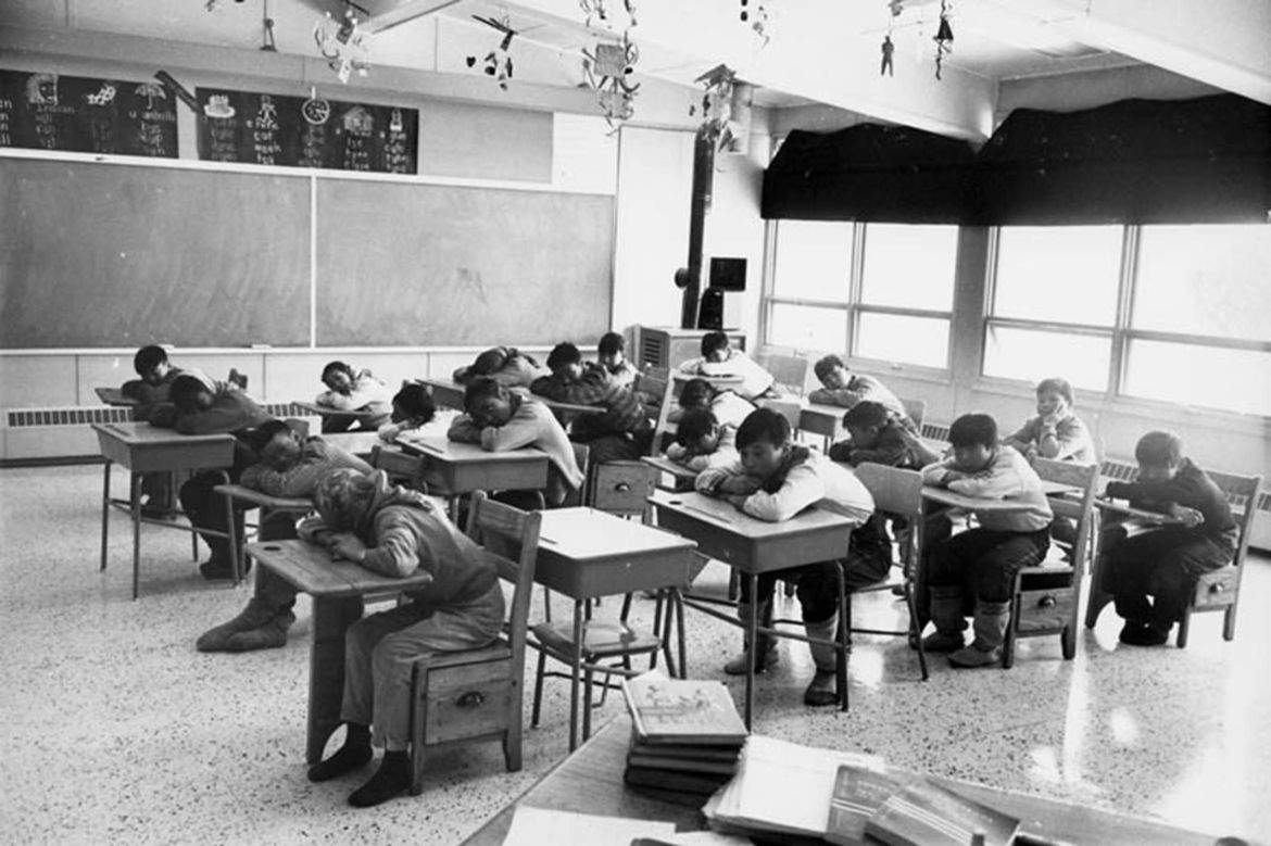 Students seated in a classroom resting their heads on their desks, Cape Dorset (Kinngait) Federal Hostel, Nunavut
