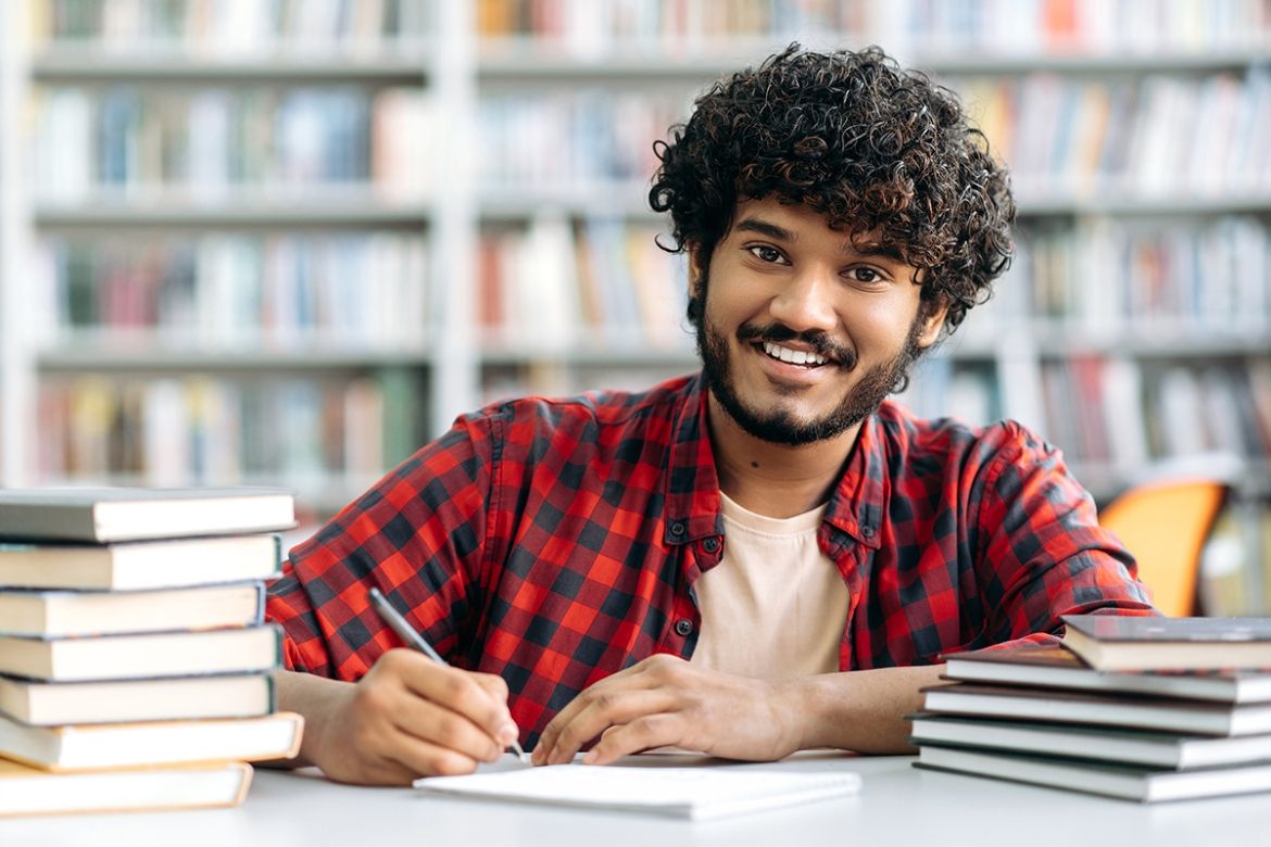 Indian man sitting in the library with books and taking notes