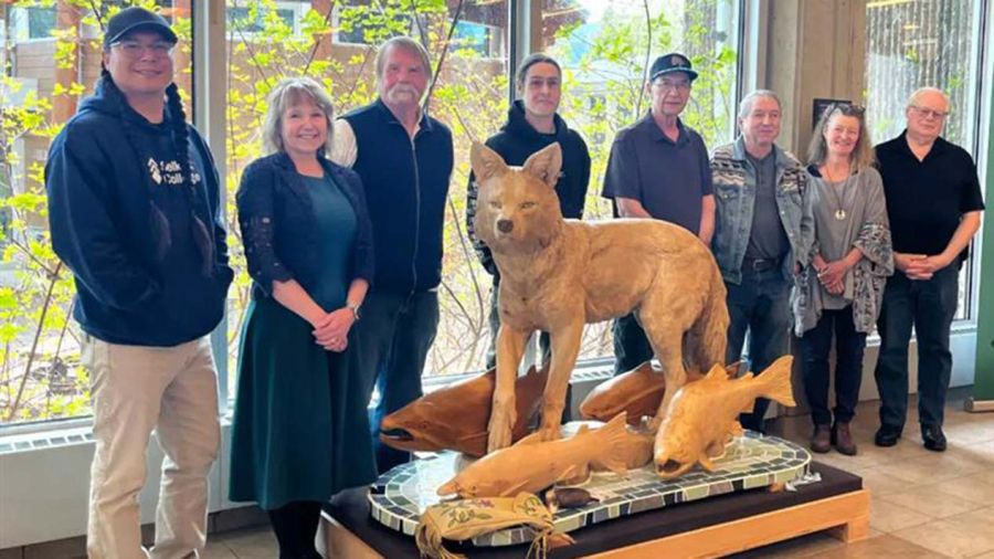 People stand around a sculpture of a coyote with salmon