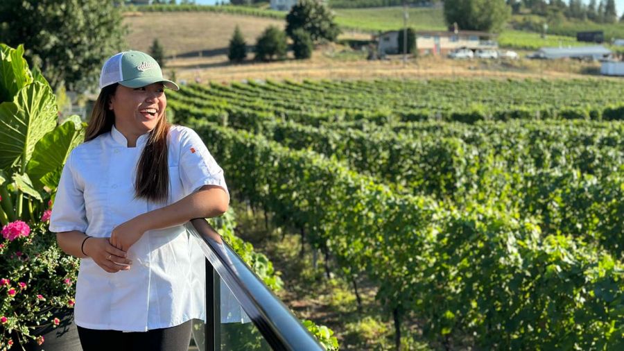 A person stands in vineyards smiling