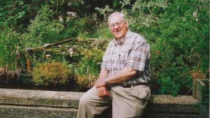Bill Merilees sits outside in a garden smiling