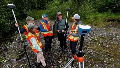 A group of interns wearing high-visibility vests stand in a circle with equipment