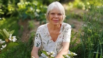 Vera Maloff crouches amid grass and flowers