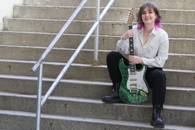 Class of 2024 co-valedictorian Jay Porteous sits on steps with her guitar.