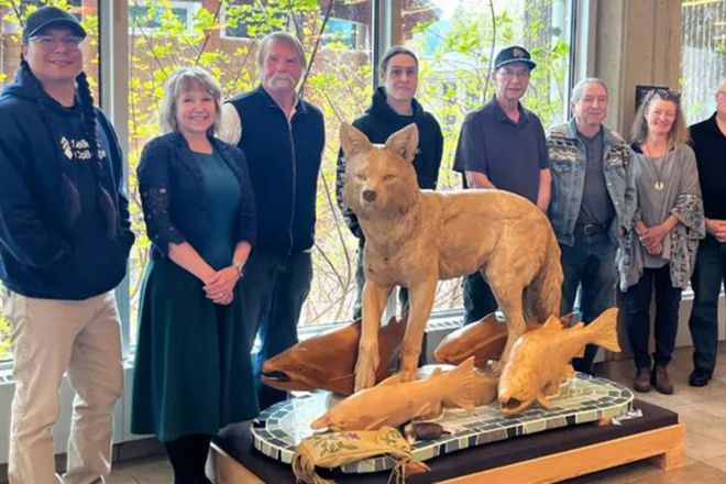 People stand around a sculpture of a coyote with salmon