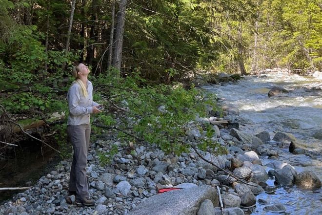 An intern stands in a rocky riverside spot operating a drone